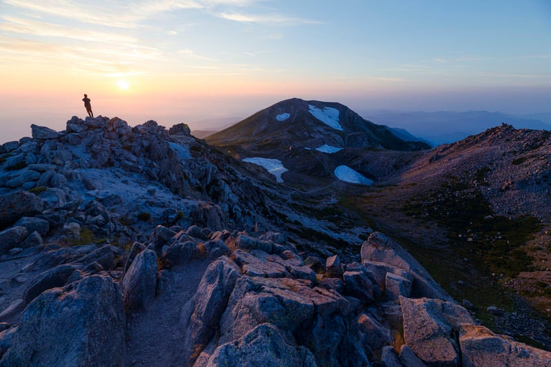 日本海に沈む夕日を眺める御前峰の登山者（白山）の写真