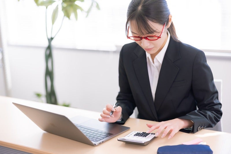 電卓で経費の計算をするメガネ女子の写真