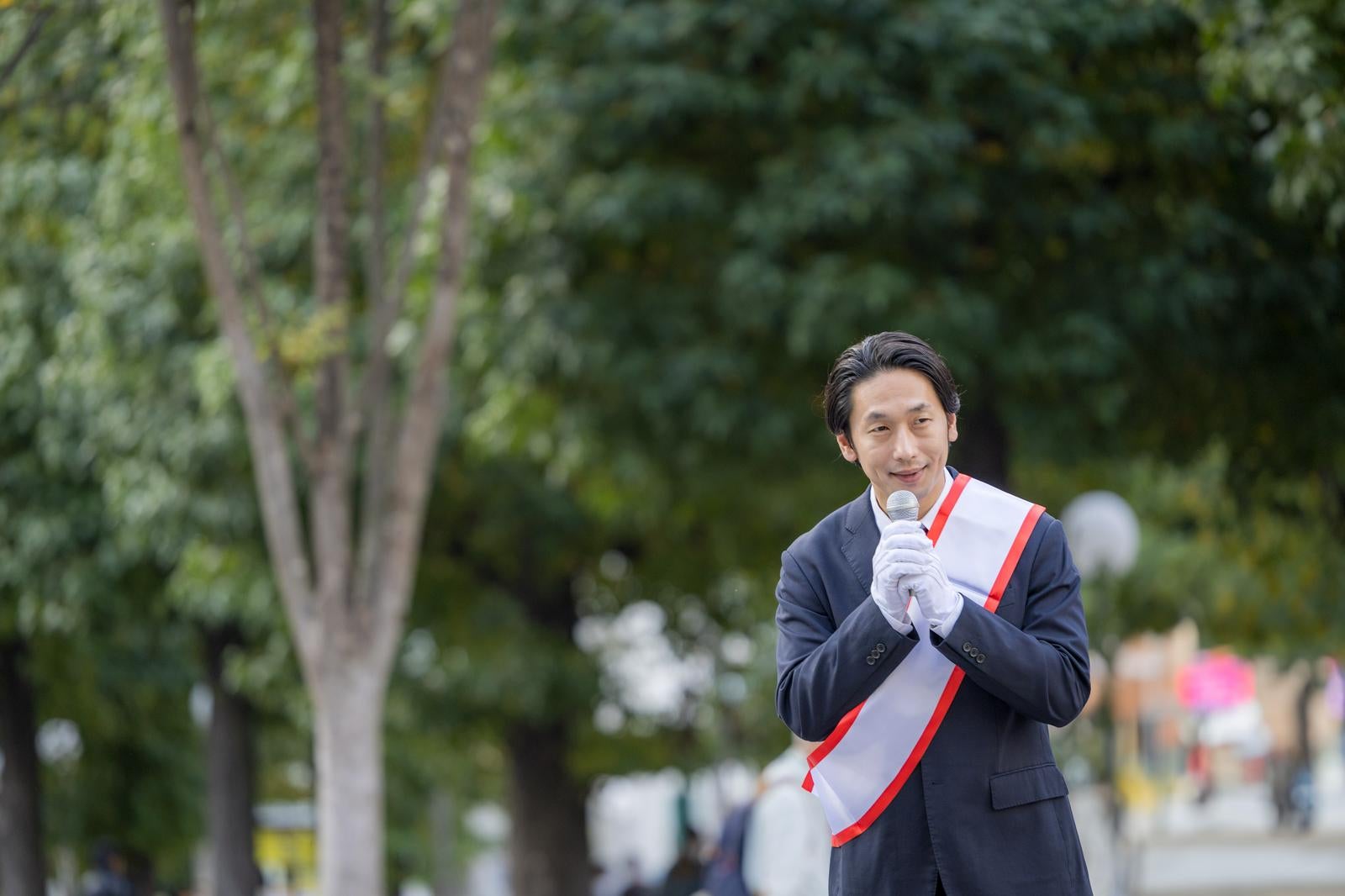 「緑豊かな公園で演説する若い男性政治家」の写真［モデル：大川竜弥］