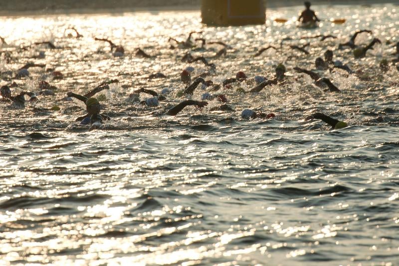 水面に光る日と競泳するトライアスロン選手の写真