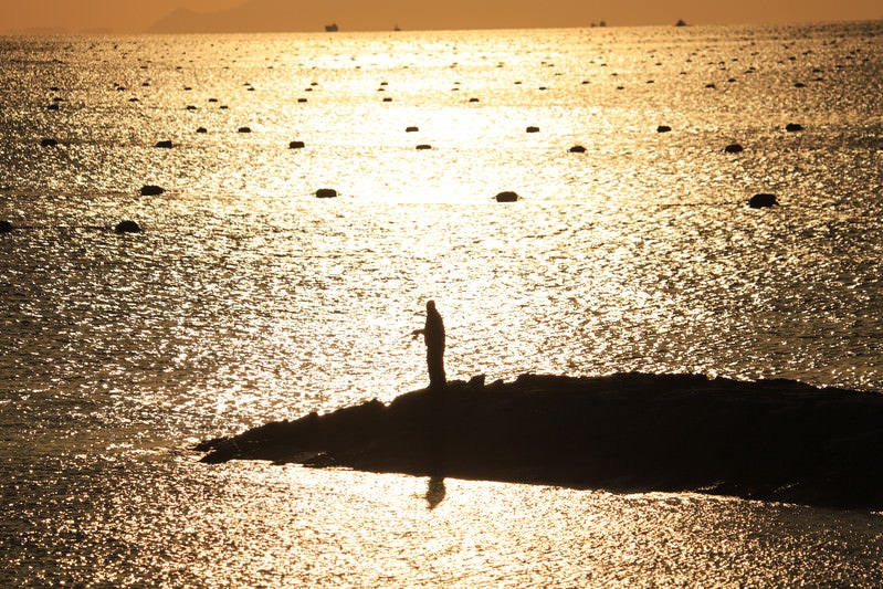 夕焼けにきらめく海と釣り人の写真