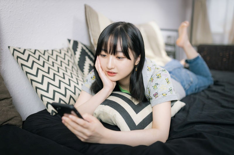 ソファーで寝転ぶスマホ女子の写真