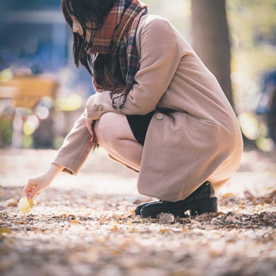 落ち葉を拾うコートの女性の写真