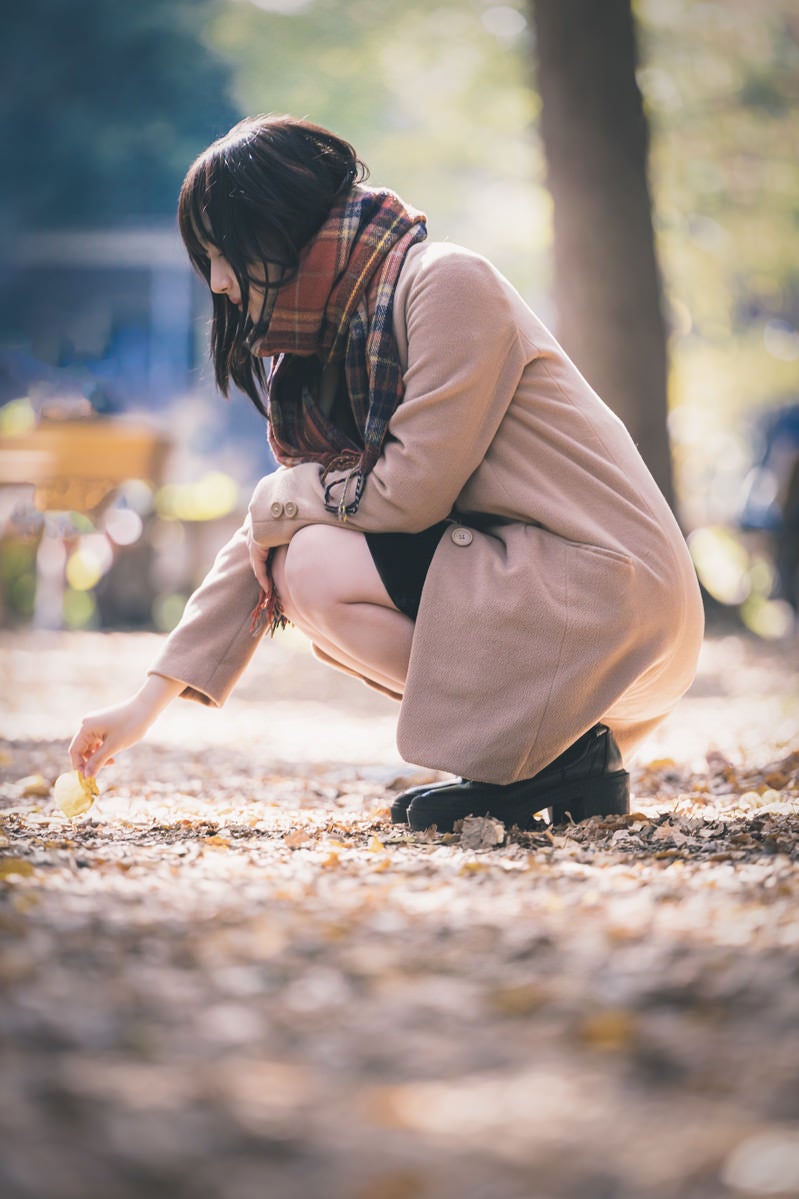 落ち葉を拾うコートの女性の写真