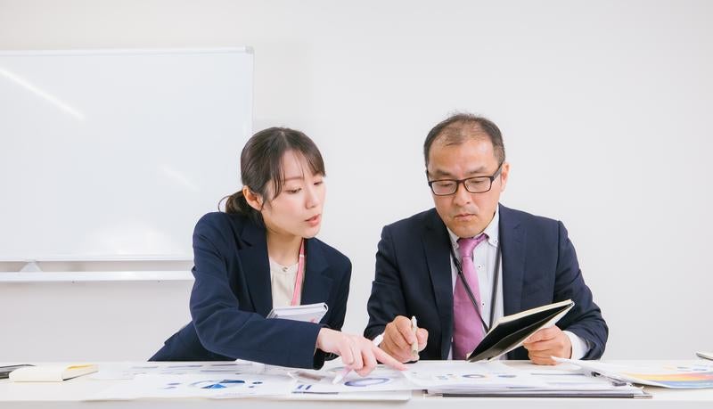 会議室で書類を確認する男女の会社員の写真