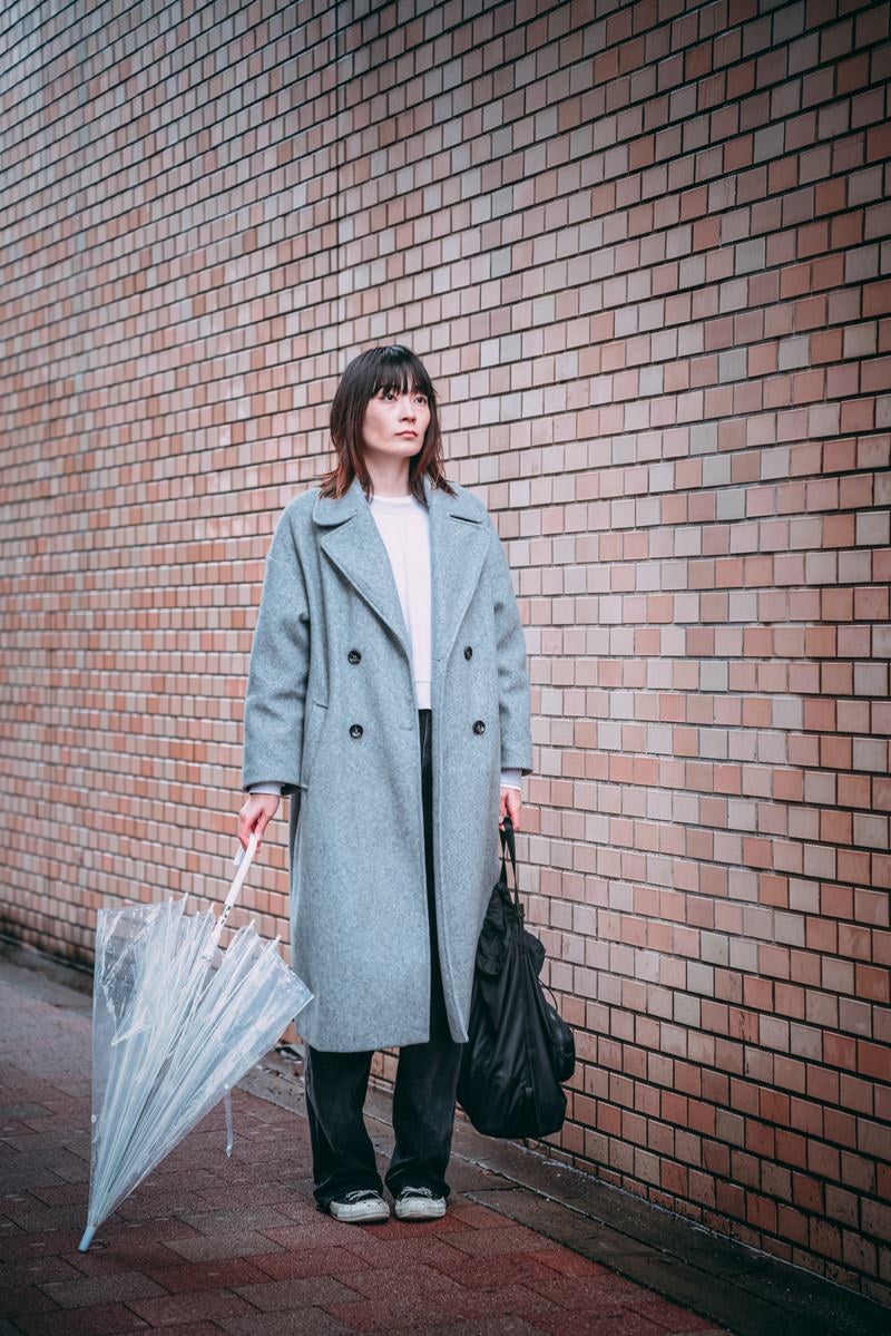 呆然と立ち尽くす雨宿り中の女性の写真