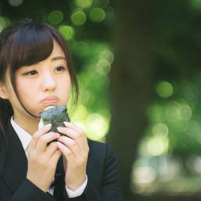 公園で孤独におにぎりを食べる就活生の写真