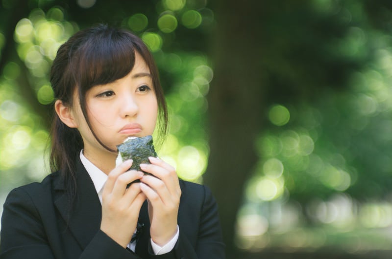 公園で孤独におにぎりを食べる就活生の写真