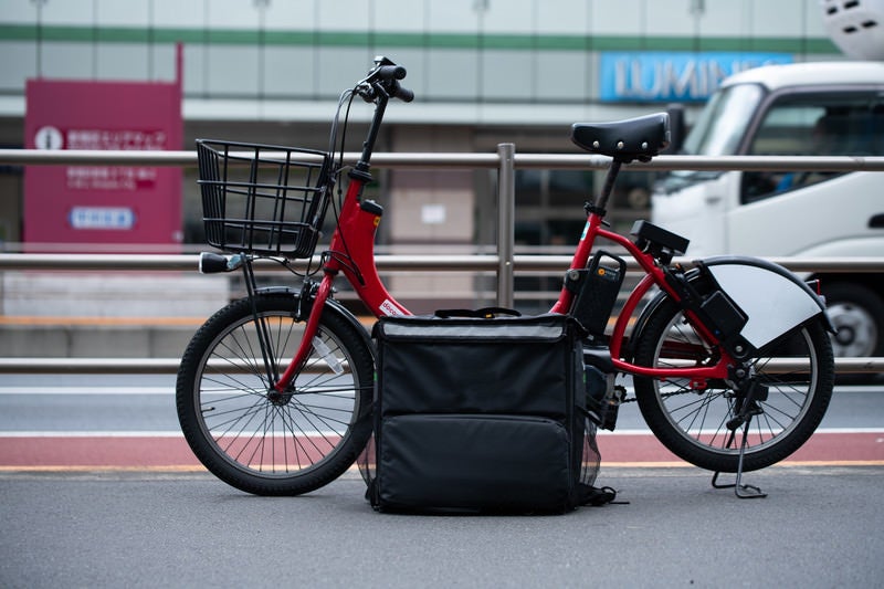 路上に止めたフードデリバリーのバッグと自転車の写真