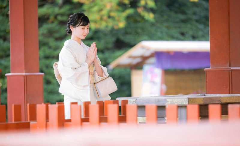 手を合わせ参拝する着物の女性の写真