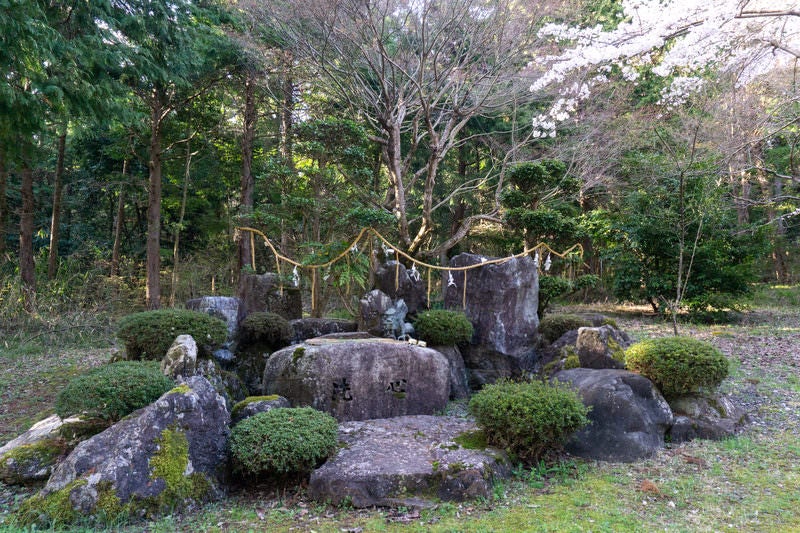 背後の木々と岩に囲まれた屋根の無い手水場の写真