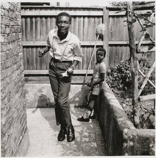 A youth dances in a garden while being watched by a child