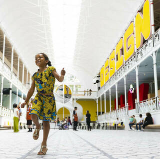 a child plays inside a spacious museum hall, the word 'design' is in big letters above them