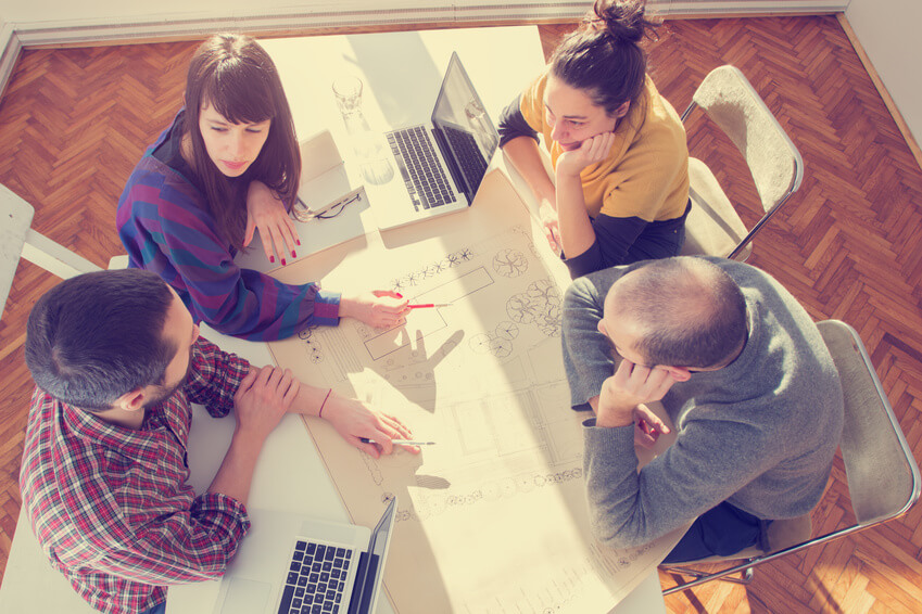 A group of people sitting around a table with laptops.