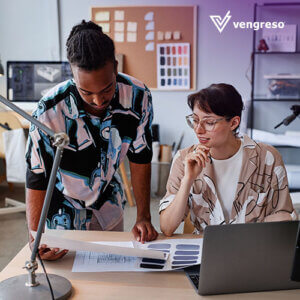 a man standing next to another on a desk in front of an open laptop learning sales tools