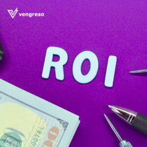 the letters ROI on a desk with the tips of pens and the tip of a hundred dollar bill