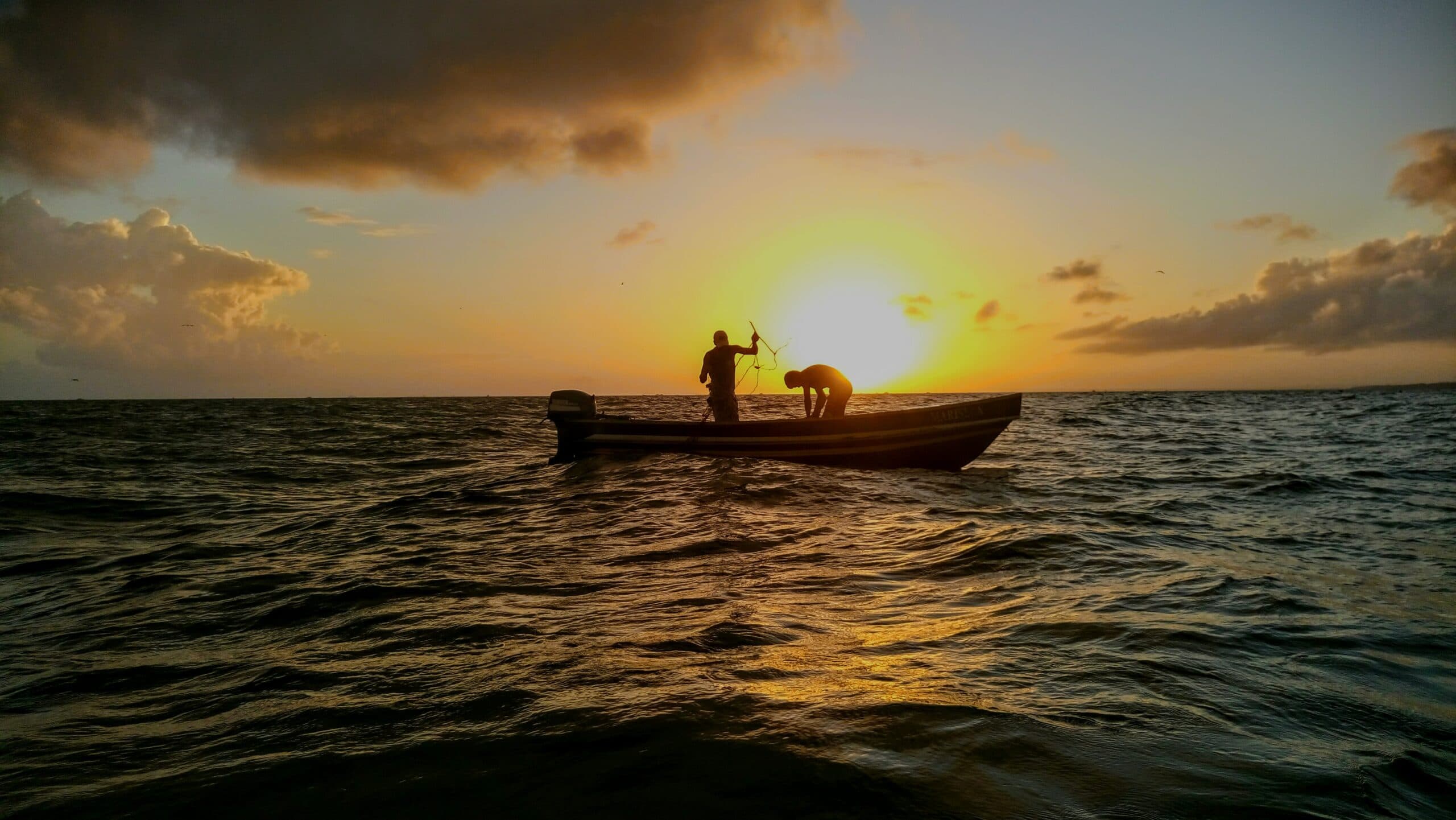 Men fishing in boat at sunset