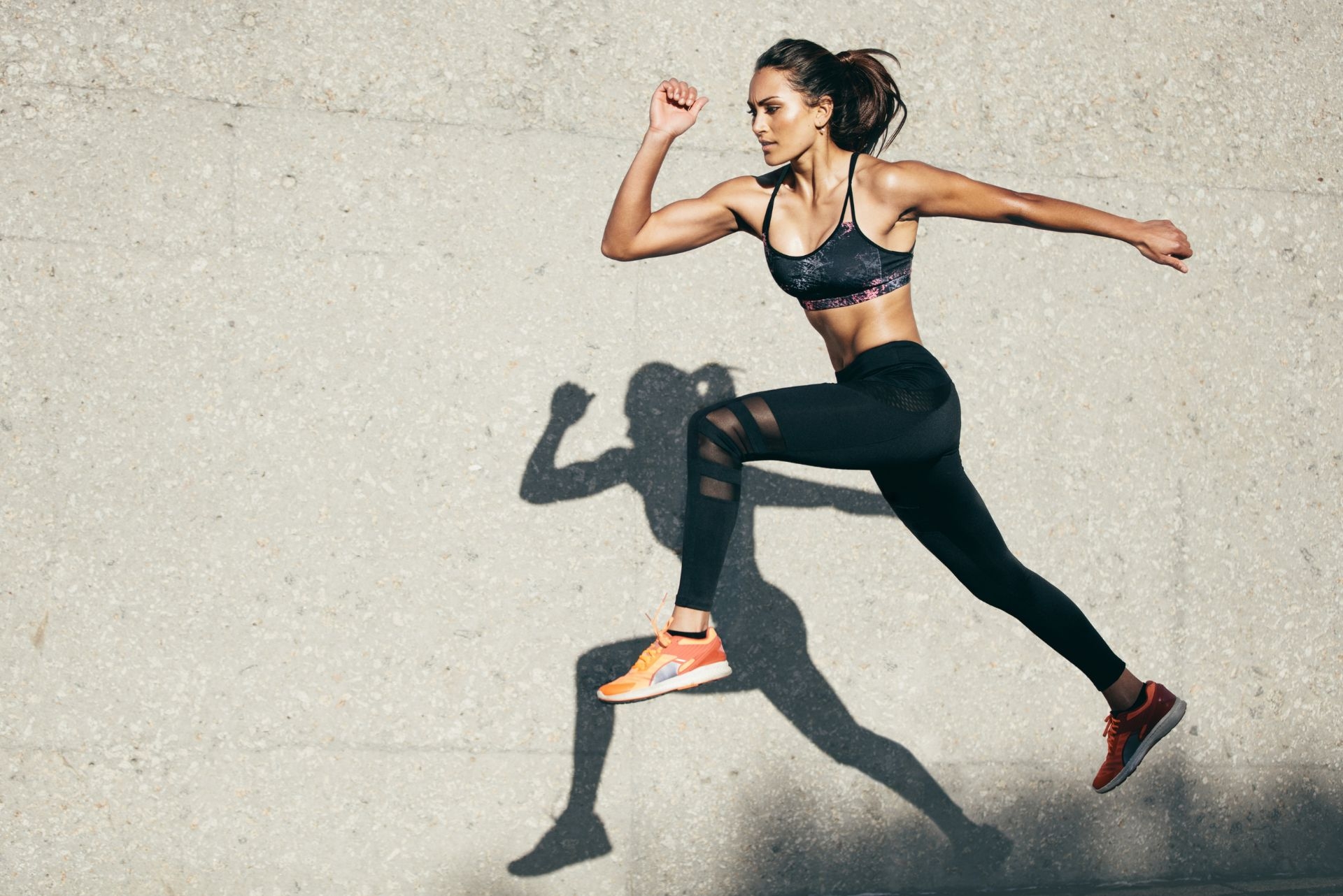 woman with fit body jumping and running against grey background 