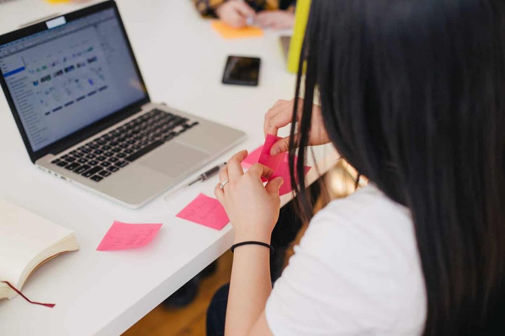 Woman writing notes on pink stickies in front of a computer.