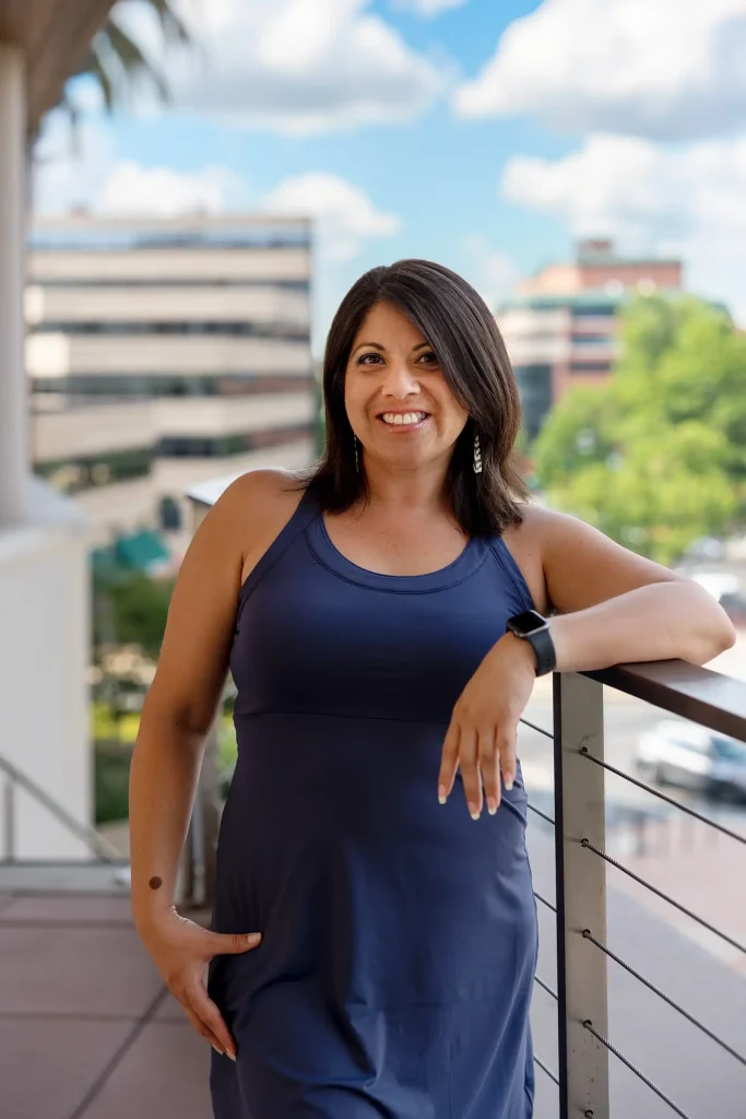 Wendie Veloz Social Impact Strategist pictured in blue dress standing against a railing. Photo by Ather Ahsan copyright 2023.