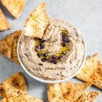 homemade olive hummus and a chip in a bowl surrounded more chips