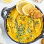 pumpkin hummus, garnished with pumpkin seeds, crackers, and lemon slices in black bowl