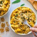 hand holding fork taking a piece of pumpkin pasta from a white bowl.