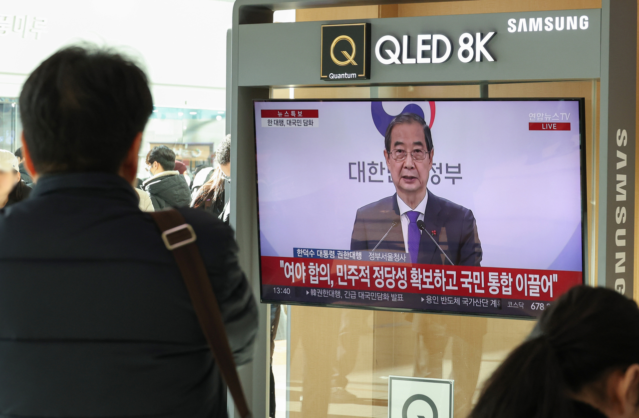 26일 오후 서울역에서 시민들이 한덕수 대통령 권한대행 국무총리 대국민 담화를 시청하고 있다. [연합]