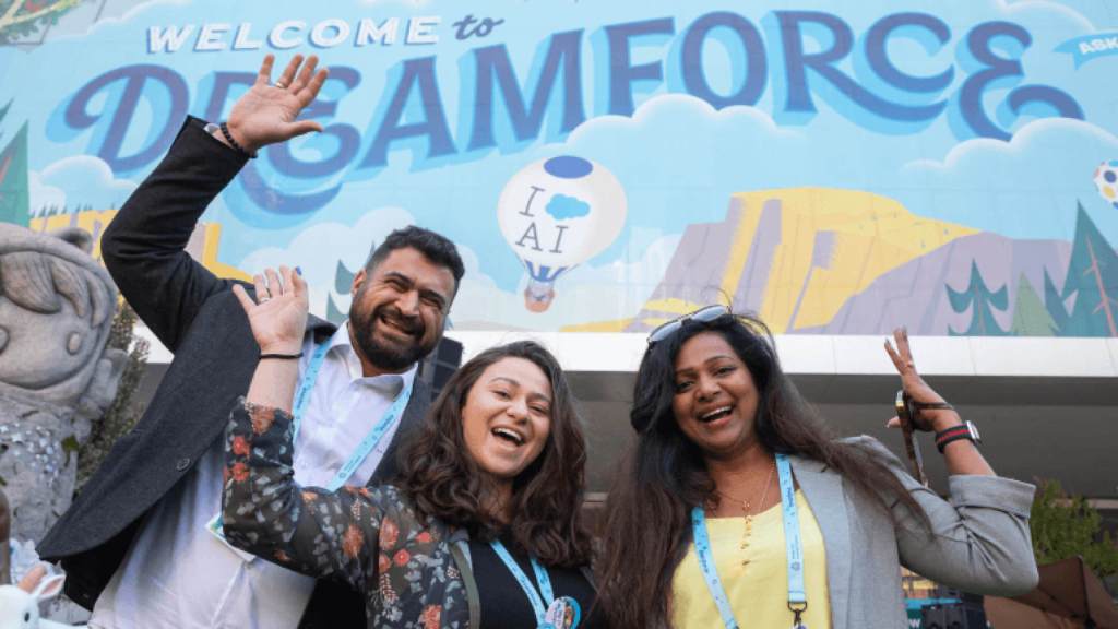 Three customers smiling under a Dreamforce sign