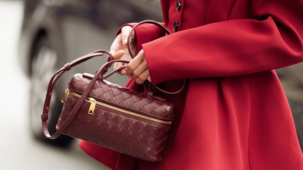 Woman holding burgundy red designer bag by bottega veneta in Paris, France, during Paris fashion week in September 2024.