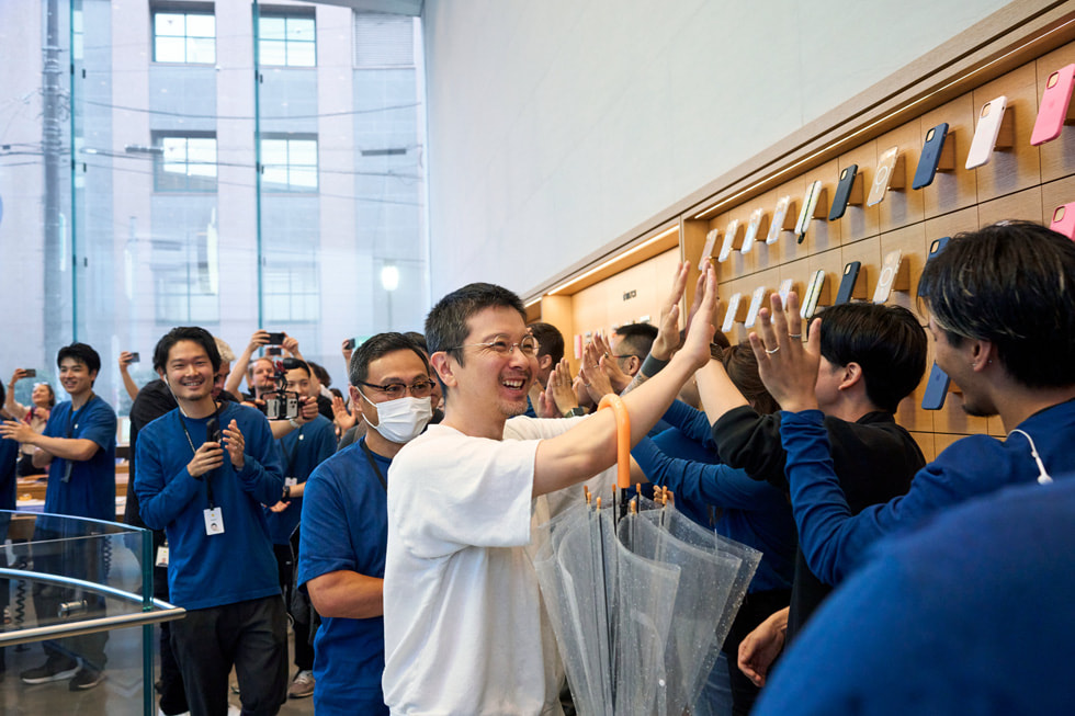 Apple 表參道零售店內，一位顧客與一排 Apple 團隊成員擊掌。