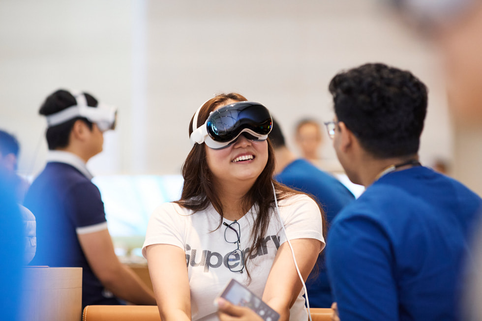 一位戴著 Apple Vision Pro 的顧客笑著與坐在她旁邊的團隊成員交談。
