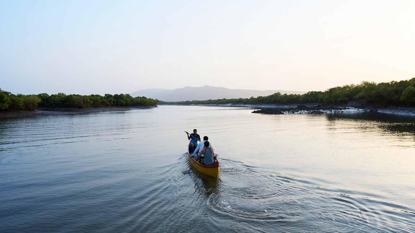 Three people in a canoe paddle down a river in Maharashtra, India.