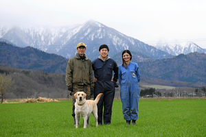 雪が解け、顔を出したばかりの小麦畑に立つえづらファームのメンバーと愛犬「キビ」=2024年4月25日午前9時4分、遠軽町白滝北支湧別、鈴木優香撮影