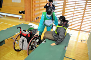 中学生に手助けしてもらい、車いすから簡易ベッドに移る記者=2024年11月14日、岩手県大槌町大槌、東野真和撮影