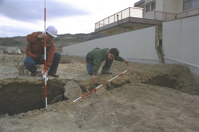 地表に現れた活断層「野島断層」のずれを調査する通商産業省地質調査所（当時）の職員。付近にはその後、野島断層保存館が整備され、後ろの壁と住宅も保存、展示されている=1995年1月19日、兵庫県北淡町（現淡路市）