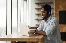 A smiling young man sits at a desk with his laptop