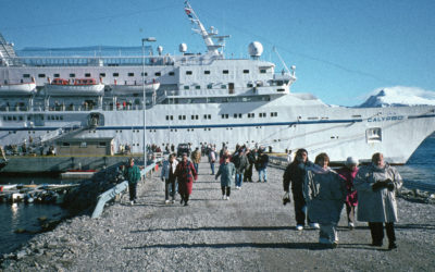 A group of people standing in front of a large ship in the water.