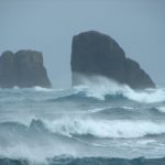 A man riding a wave on top of haystack rock.