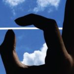 A close up of a hand with a blue cloudy sky.