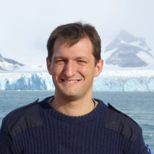 A person standing in front of a body of water posing for the camera.