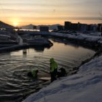 A sunset over a body of water with buildings in the snow.