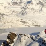 People on a snowy mountain range holding a rainbow flag