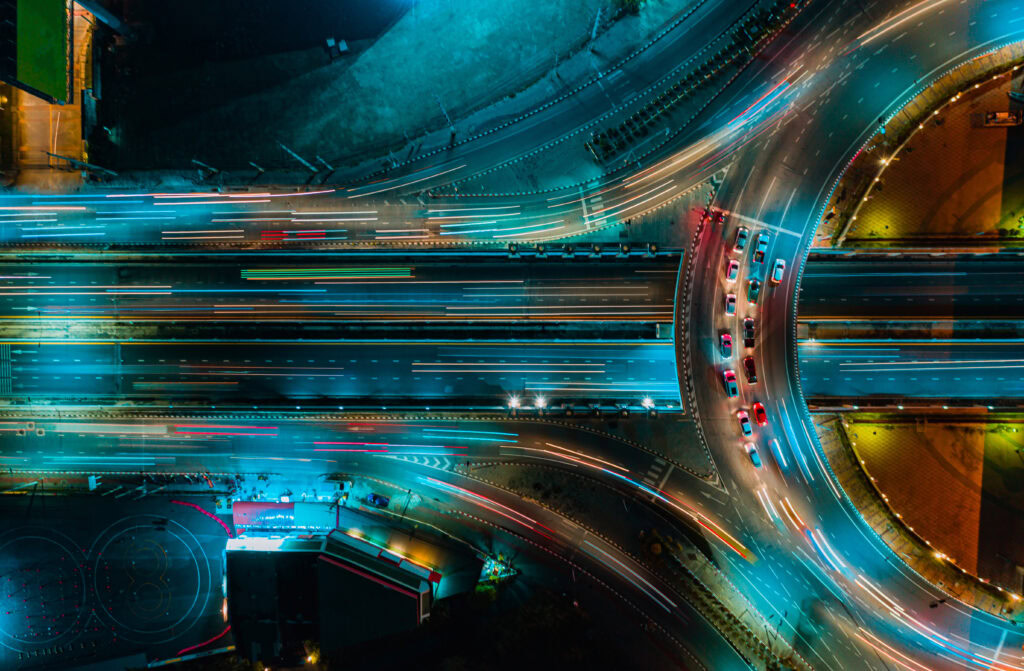 Aerial view of a bustling, multi-lane intersection at night with illuminated streets, moving traffic, and vibrant light trails from vehicles—capturing the essence of urban energy akin to an Asset Analytics snapshot in real time.