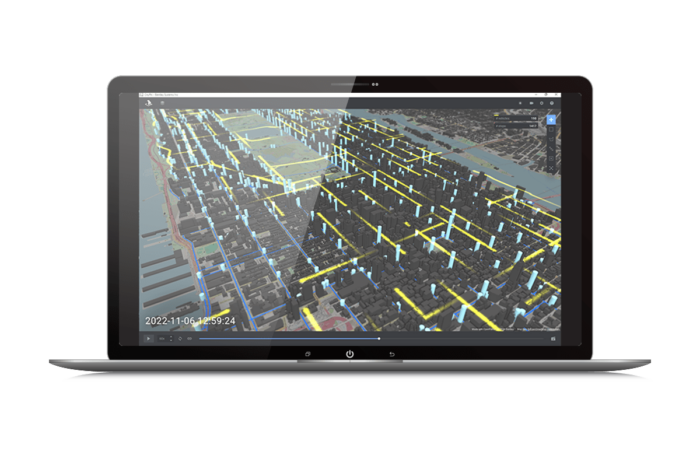 Laptop screen showing a 3D map with highlighted buildings and grid lines. The bottom left corner displays a timestamp: "2022-11-06 21:59:24.