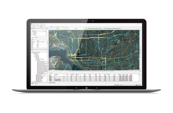 A laptop screen displaying a detailed geographic information system (GIS) map with various color-coded lines and data tables.