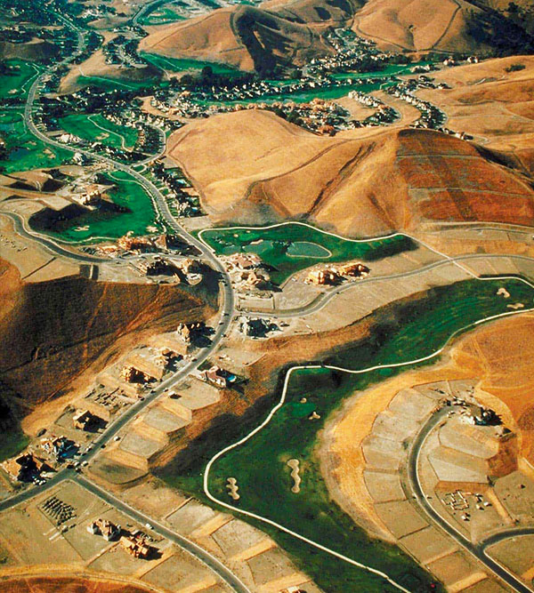 Aerial view of a developing suburban area with roads, homes, and surrounding hilly terrain