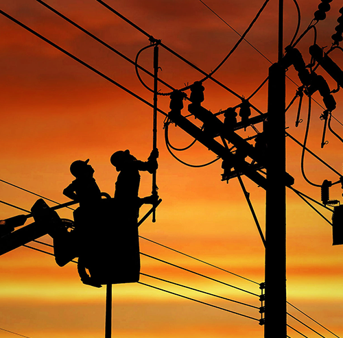 Stockfoto: Silhouette von zwei Elektrikern, die auf einem Kranwagen arbeiten, um ein elektrisches Getriebe auf einem Strommast zu installieren