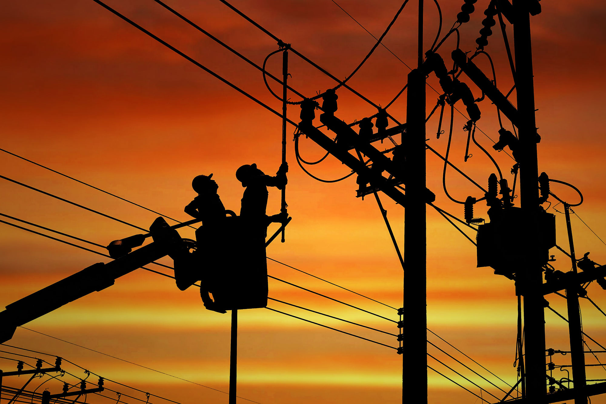 Stockfoto: Silhouette von zwei Elektrikern, die auf einem Kranwagen arbeiten, um ein elektrisches Getriebe auf einem Strommast zu installieren