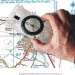 A hand holding a compass over a map